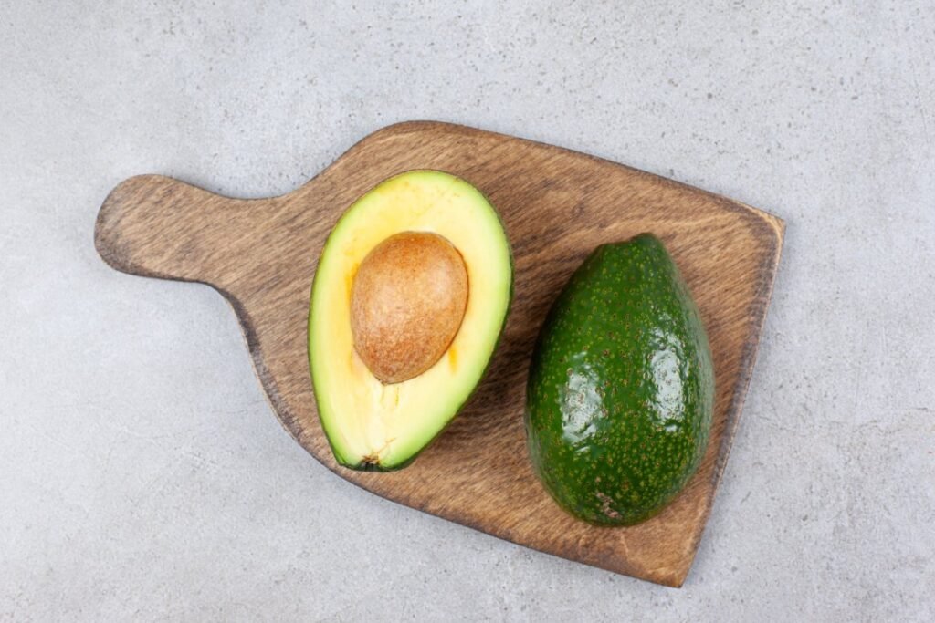 Fresh whole avocado and sliced half showing green flesh and seed on white background